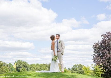 A bride and groom stand in the grass.