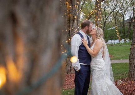 A bride and groom kissing in front of trees.