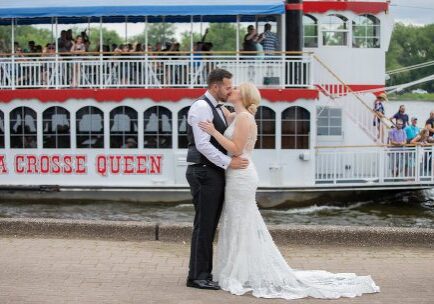 A bride and groom kiss in front of the boat.