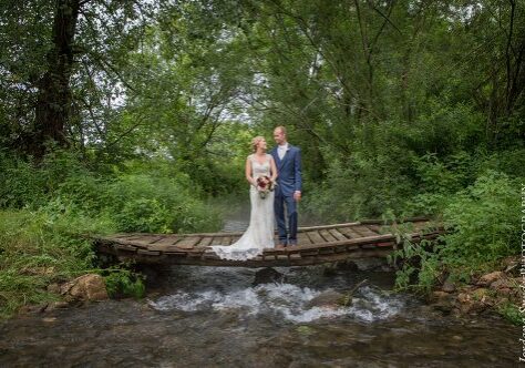 A bride and groom standing on a bridge over water.
