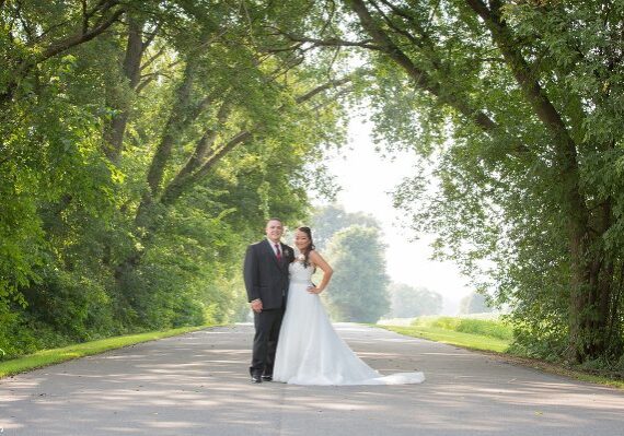 A bride and groom pose for a picture on the side of a road.