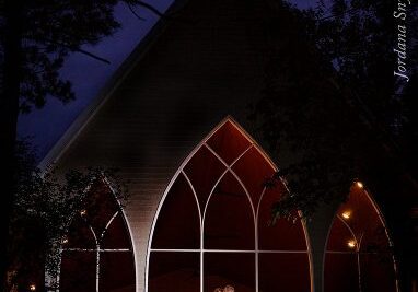 A bride and groom standing in front of a church at night.