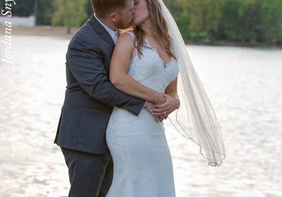 A bride and groom kissing in front of the water.