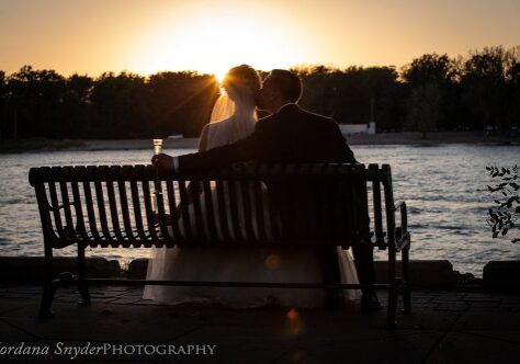 A couple sitting on top of a bench at sunset.