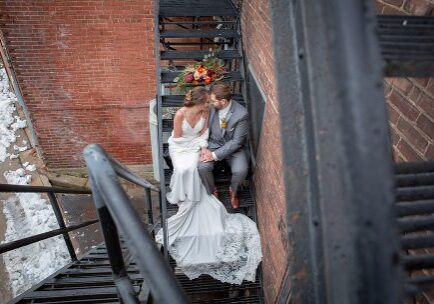 A bride and groom sitting on stairs in front of a brick wall.