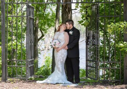A bride and groom pose for a picture in the woods.