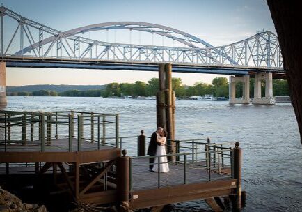A bride and groom standing on the dock of a pier.