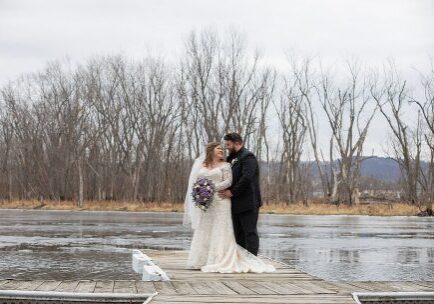 A bride and groom standing on the edge of a pier.
