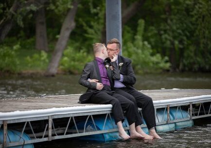 Two men sitting on a dock next to water.
