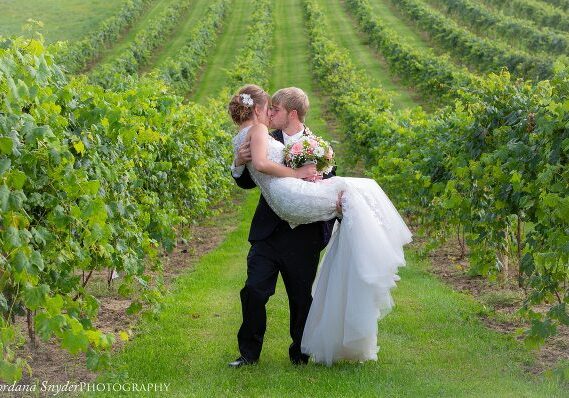 A bride and groom kissing in the middle of a vineyard.