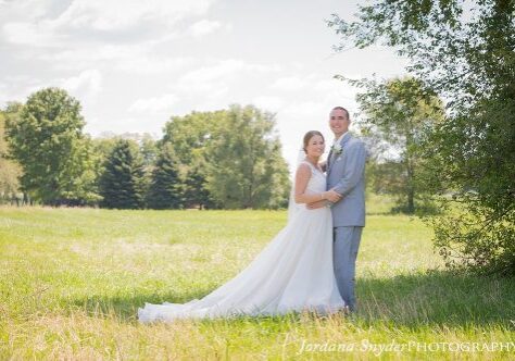 A bride and groom pose for a picture in the grass.