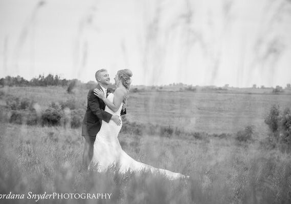 A black and white photo of a bride and groom in the grass.