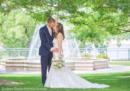 A bride and groom kissing in front of a fountain.
