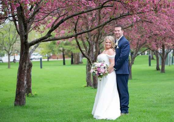 A bride and groom pose for a picture in the park.