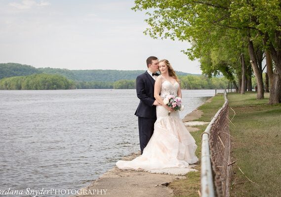 A bride and groom standing next to the water.