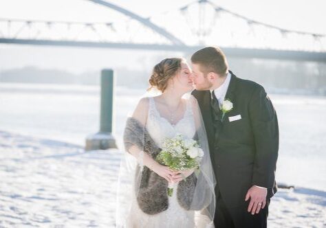 A bride and groom kissing in front of the water.