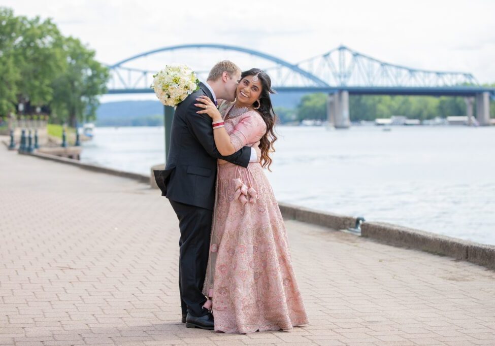 A man and woman in formal wear kissing on the side of a river.